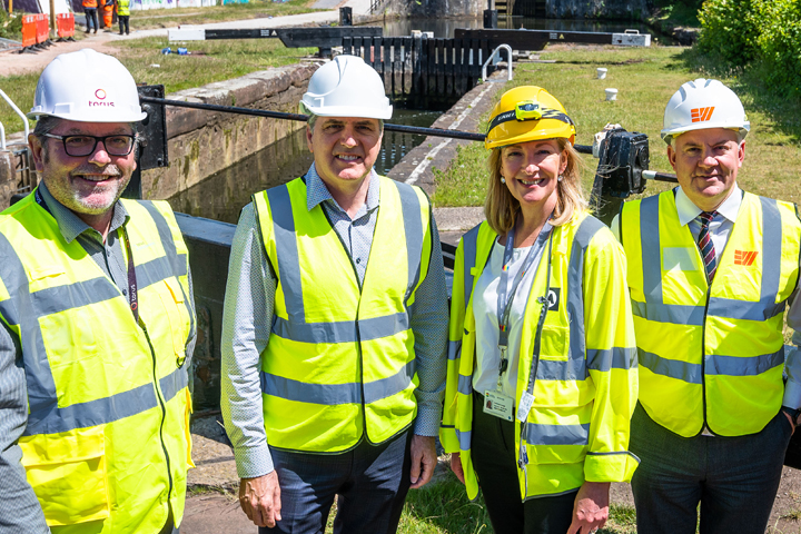 Photo of a group of people wearing high visibility jackets and hard hats, smiling and facing the camera