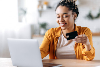 Photo of someone sat using a laptop at a table while holding a credit card