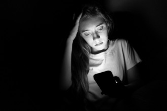 A black and white photo of a young woman on her mobile phone, her face being lit by the screen