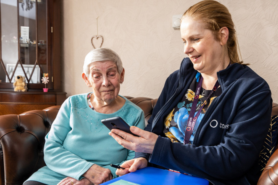 Photo of two people sat down while one shows the other something on her mobile phone